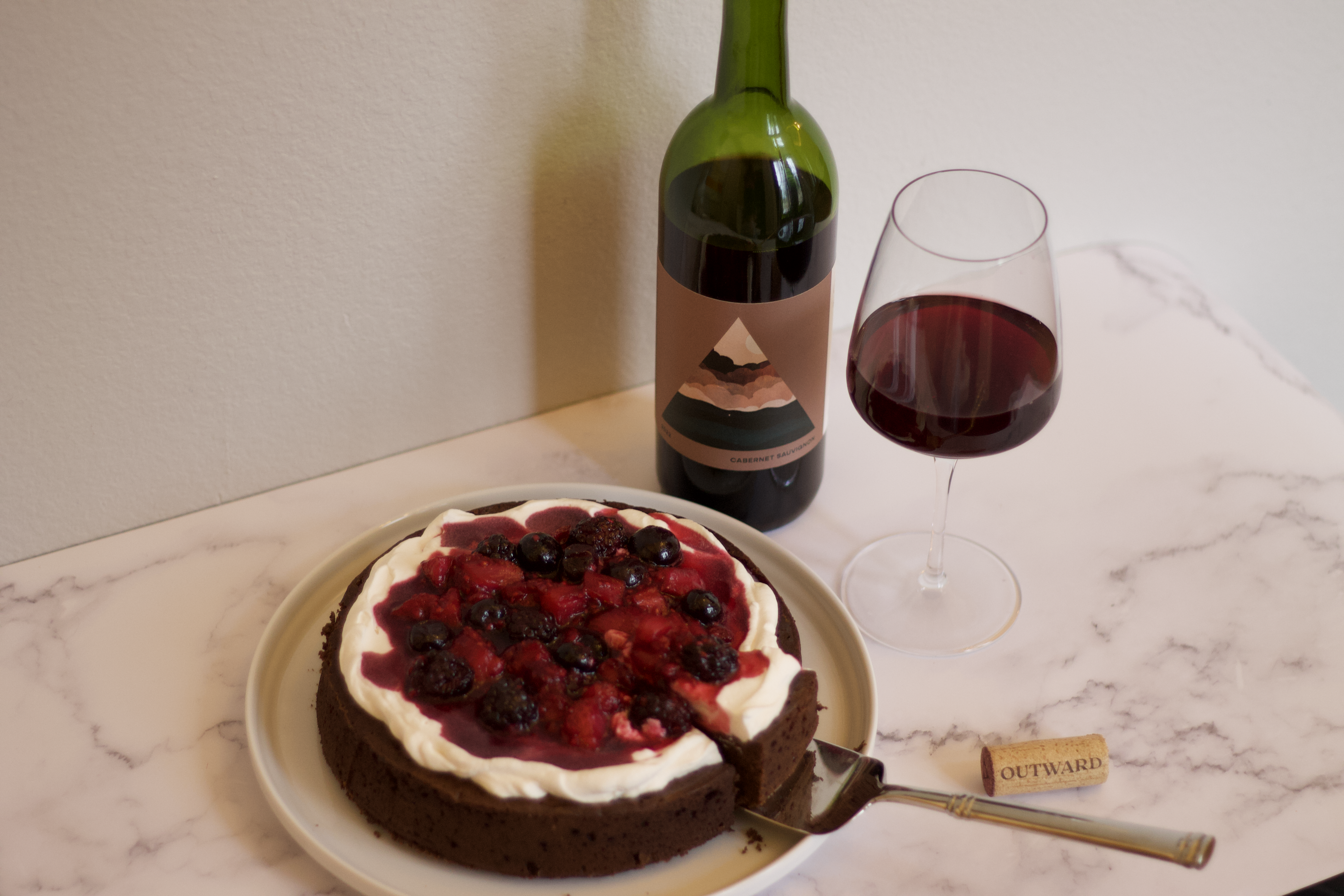 Flourless chocolate cake with berry compote next to a bottle of outward wine and a poured glass of red wine